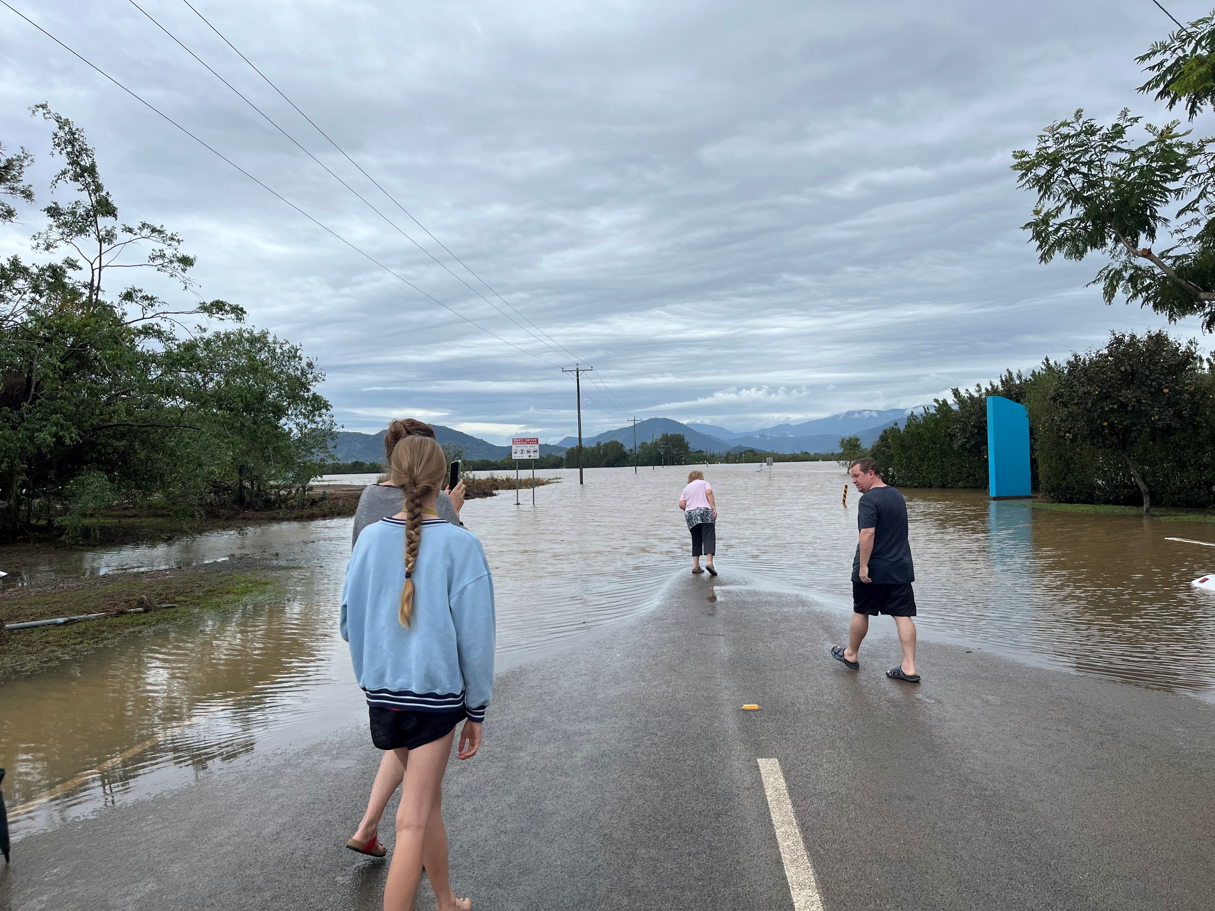 A bunch of people stand on a dry section of road that is completely flooded ahead of them.