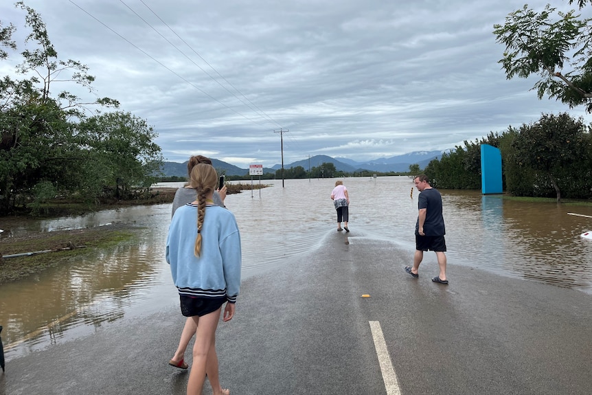 A bunch of people stand on a dry section of road that is completely flooded ahead of them.