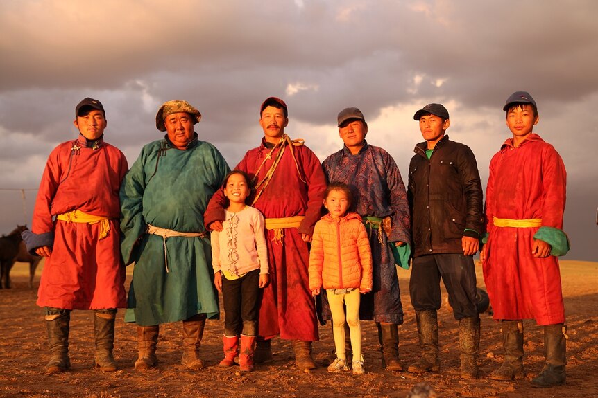 Six Mongolian men stand in the Gobi Desert in robes with two Mongolian girls.