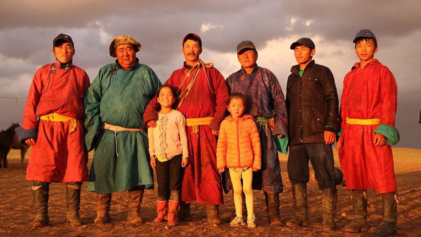 Six Mongolian men stand in the Gobi Desert in robes with two Mongolian girls.