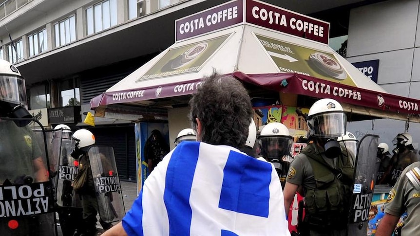 Protester fronts riot police in Greece wearing Greek flag