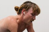 Close up of para cyclist Alistair Donohoe who is shirtless, with air pods, sweating, as he trains in a climate chamber