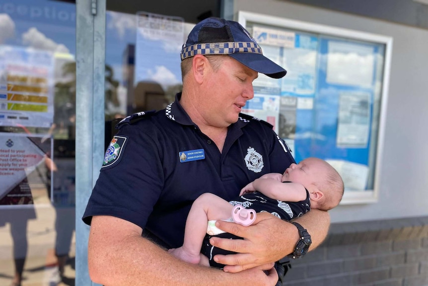 A police officer stands in uniform holding a baby.