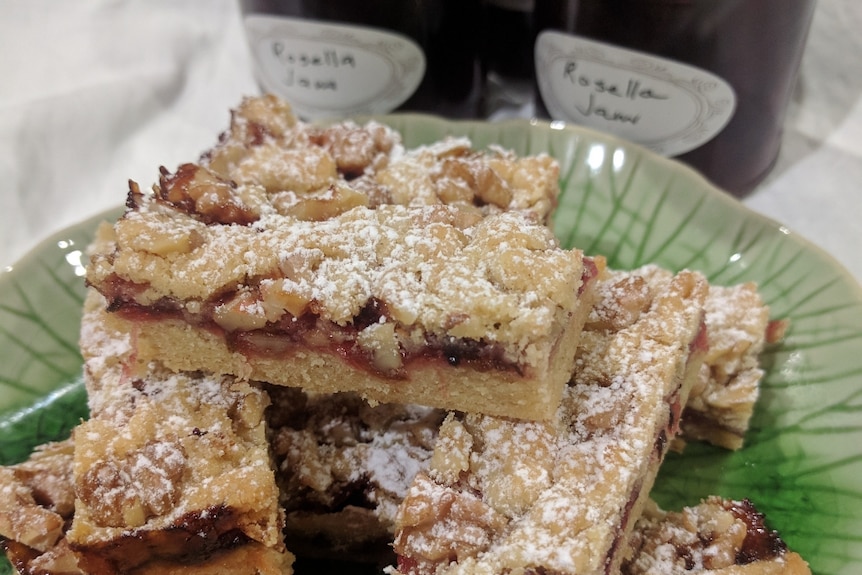 Rosella jam and pecan slice on a green plate with jars of jam in the background.