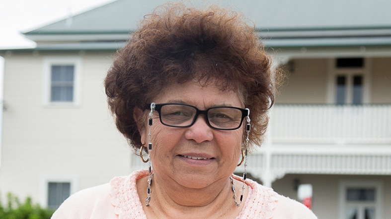 Woman with glasses photographed from waist up in front of building.