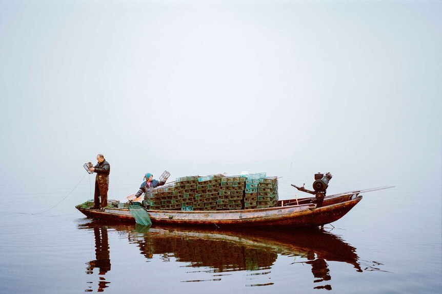 A Chinese couple prepare crates to throw into the water off their boat.
