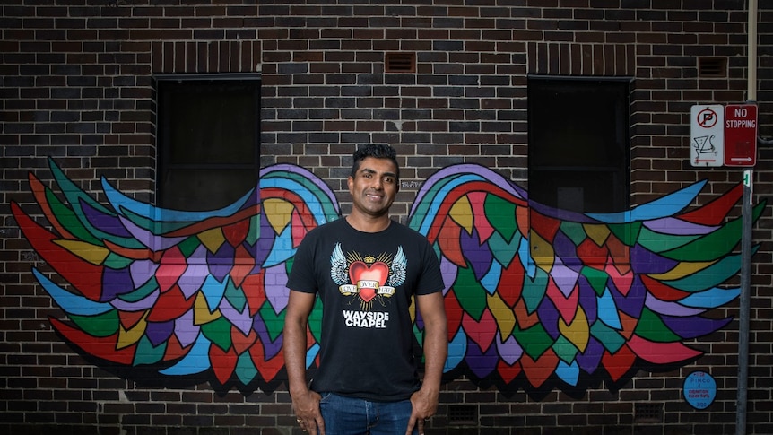 A man stands in front of a wall with wings painted on it.