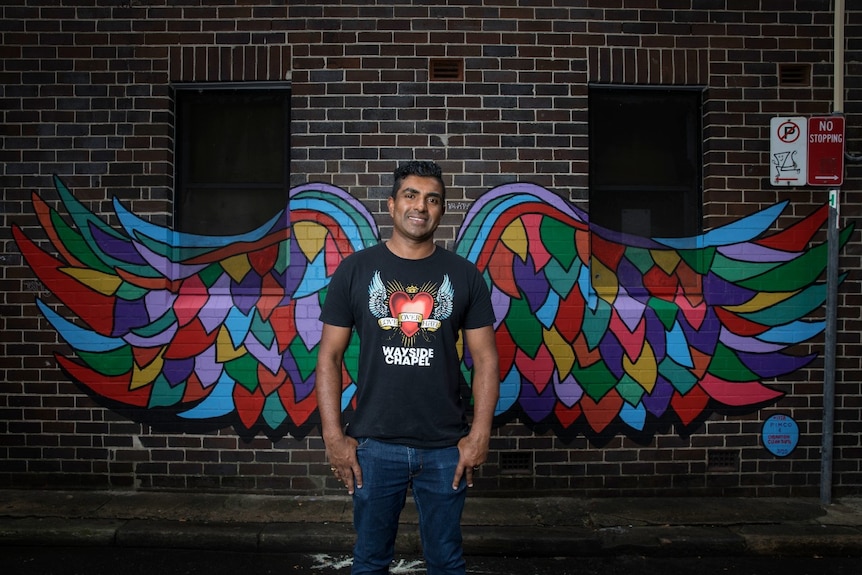 A man stands in front of a wall with wings painted on it.