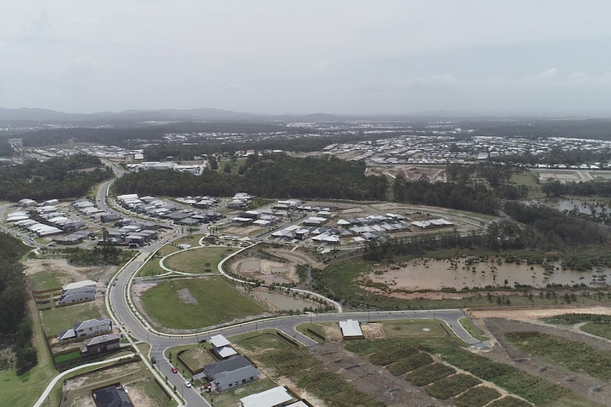 Aerial of housing estate, roads and looking toward mountains in the distance.