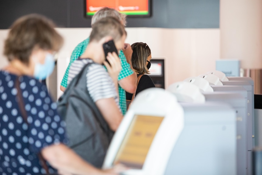 A line of people use self check in machines at Perth Airport.