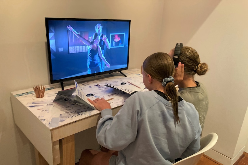 Two girls look at a screen with a man dancing on it