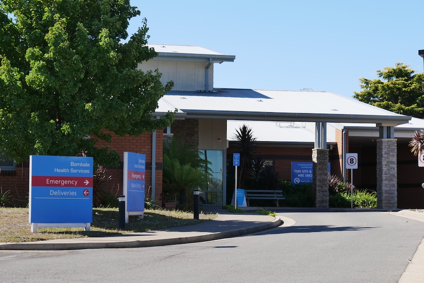 a building of a hospital with a sign out the front and a car park in the foreground