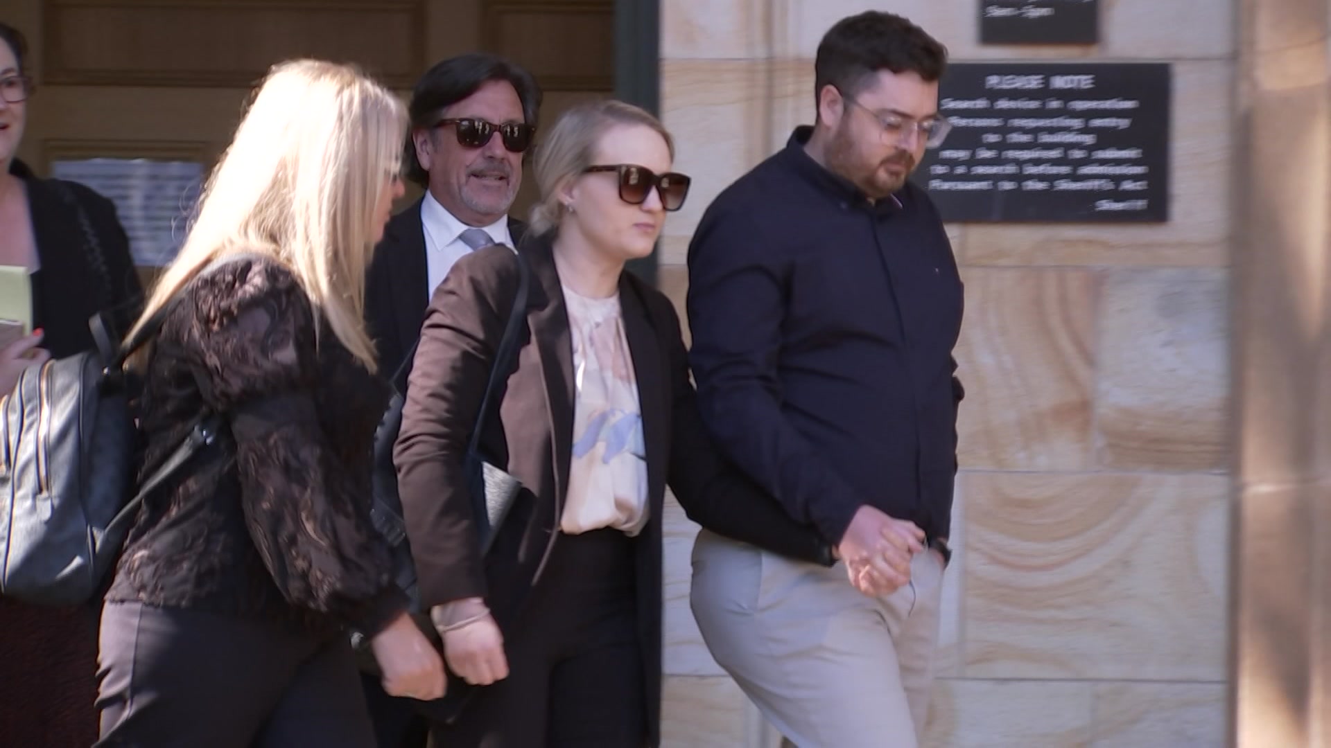 a man and a woman walk hand-in-hand out of a building next to a group of people