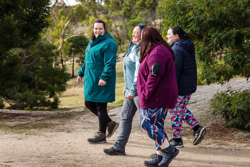 Four people in warm jackets and activewear tights walk through the open bush, smiling widely.