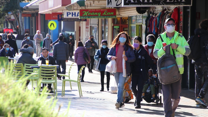 People wearing masks walk on a footpath.