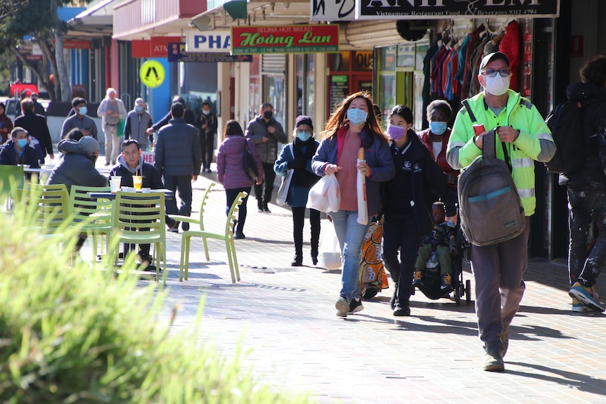 People wearing masks walk on a footpath.