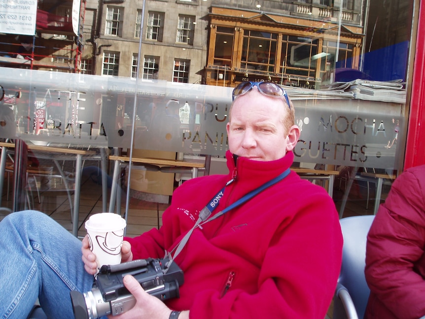 Stephen Mitchell sits at a cafe holding a take-away coffee cup.