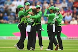 A bowler with her back to the camera is hugged by happy teammates after her wicket in a game of The Hundred..