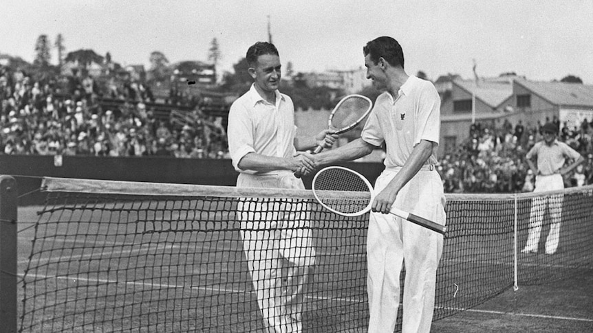 A black and white photo of two tennis players who are shaking hands at the court net, both are holding tennis racquets