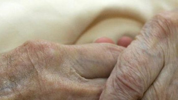 A young carer holds the hands of an elderly woman in a nursing home.