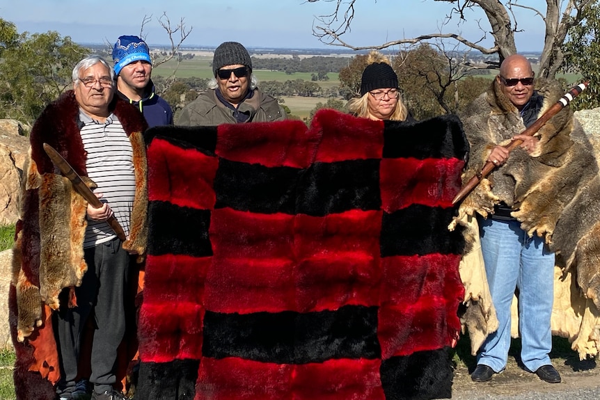 A group of people wearing skins and holding a black and red chequered banner.