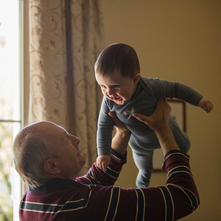 A grandfather lifts a small smiling child into the air.