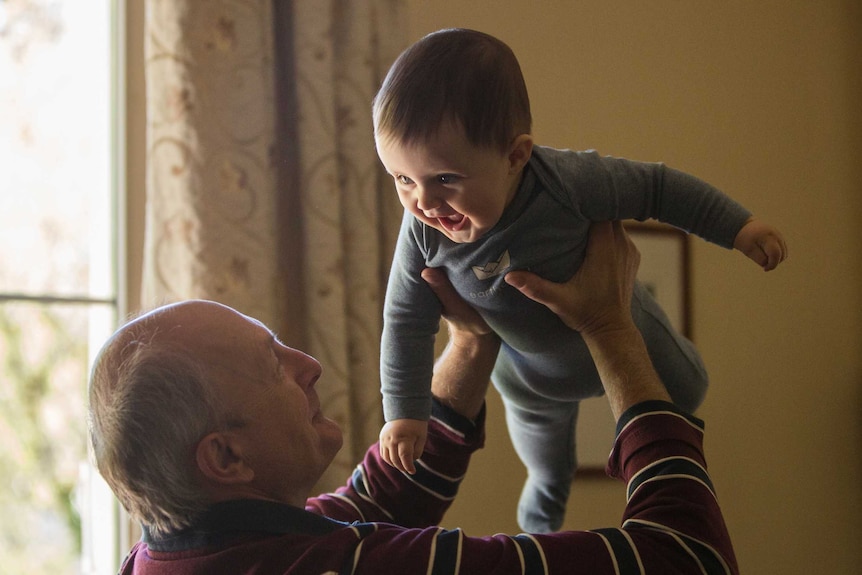 A grandfather lifts a small smiling child into the air.