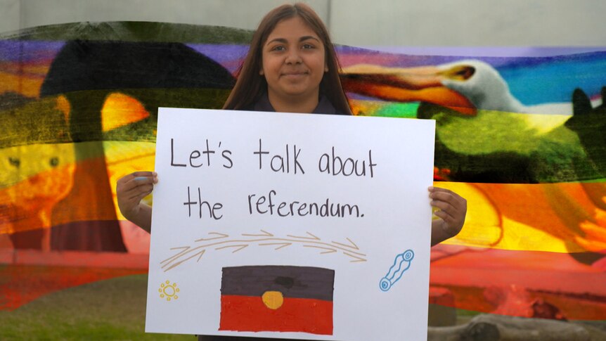 An Indigenous person holds up a sign saying "Let's talk about the referendum".