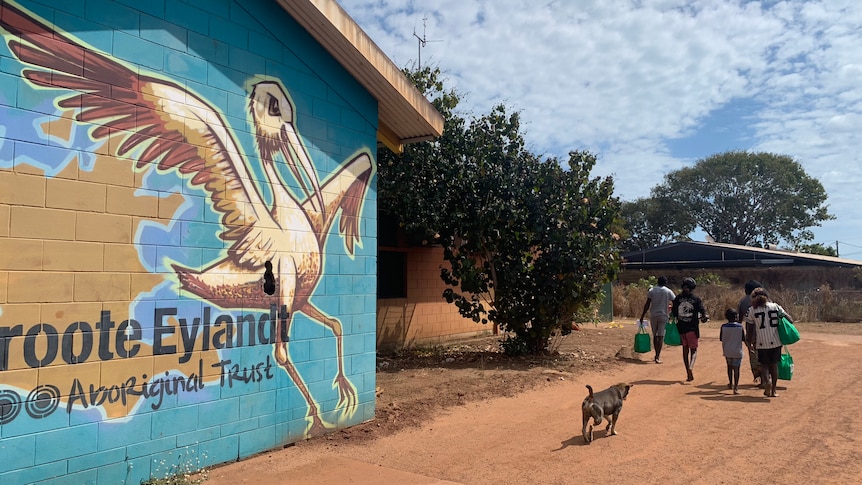 A mural of Groote Eylandt with a map and a bird on the side of a building as locals walk past.