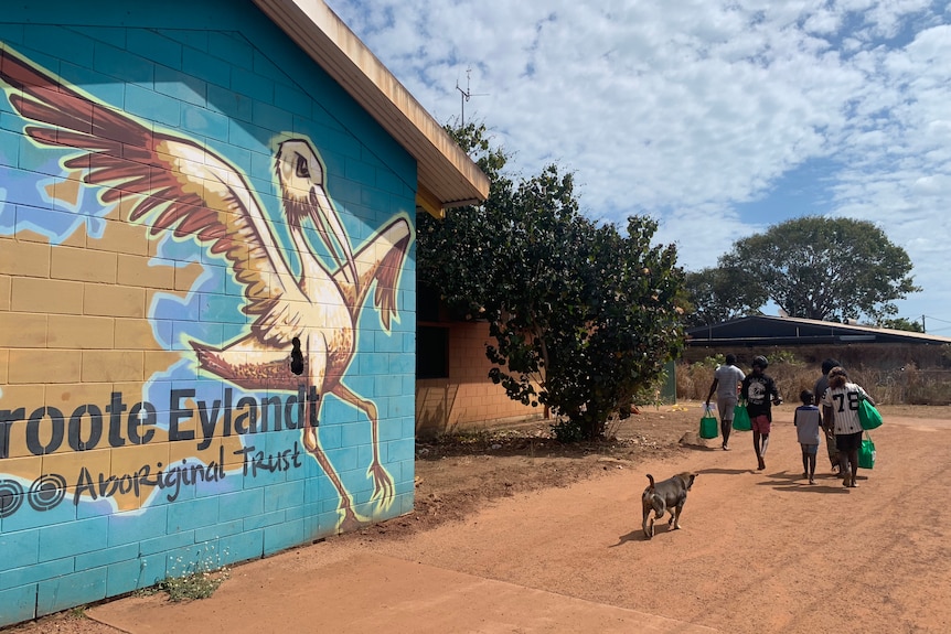 A mural of Groote Eylandt with a map and a bird on the side of a building as locals walk past.