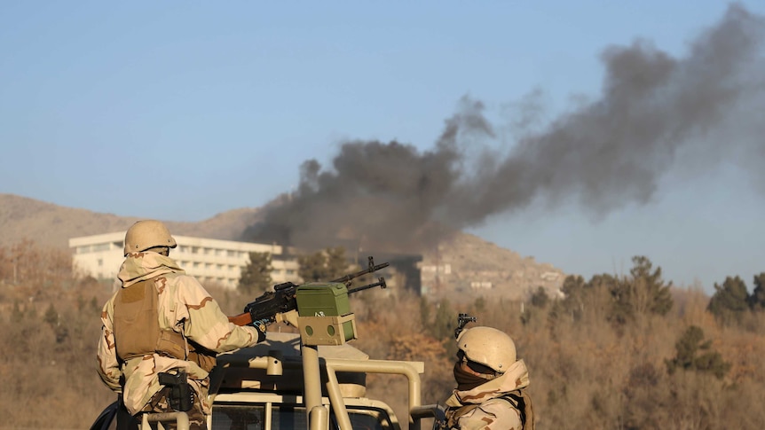 Smoke rises from the Intercontinental Hotel in Kabul. Afghan security personnel watch on from behind a gun on a vehicle.