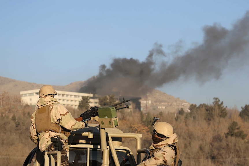 Smoke rises from the Intercontinental Hotel in Kabul. Afghan security personnel watch on from behind a gun on a vehicle.