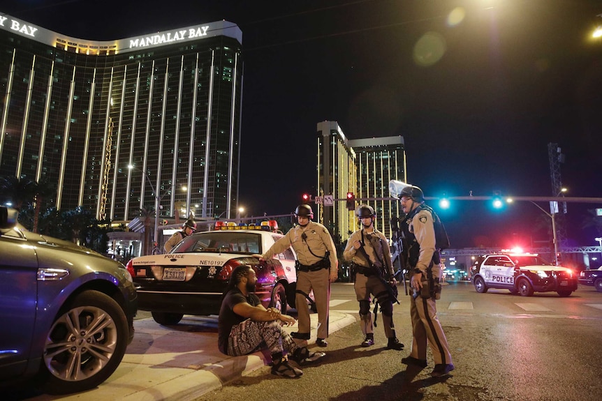 Police officers stand outside the Mandalay hotel and speak to a man on the curb