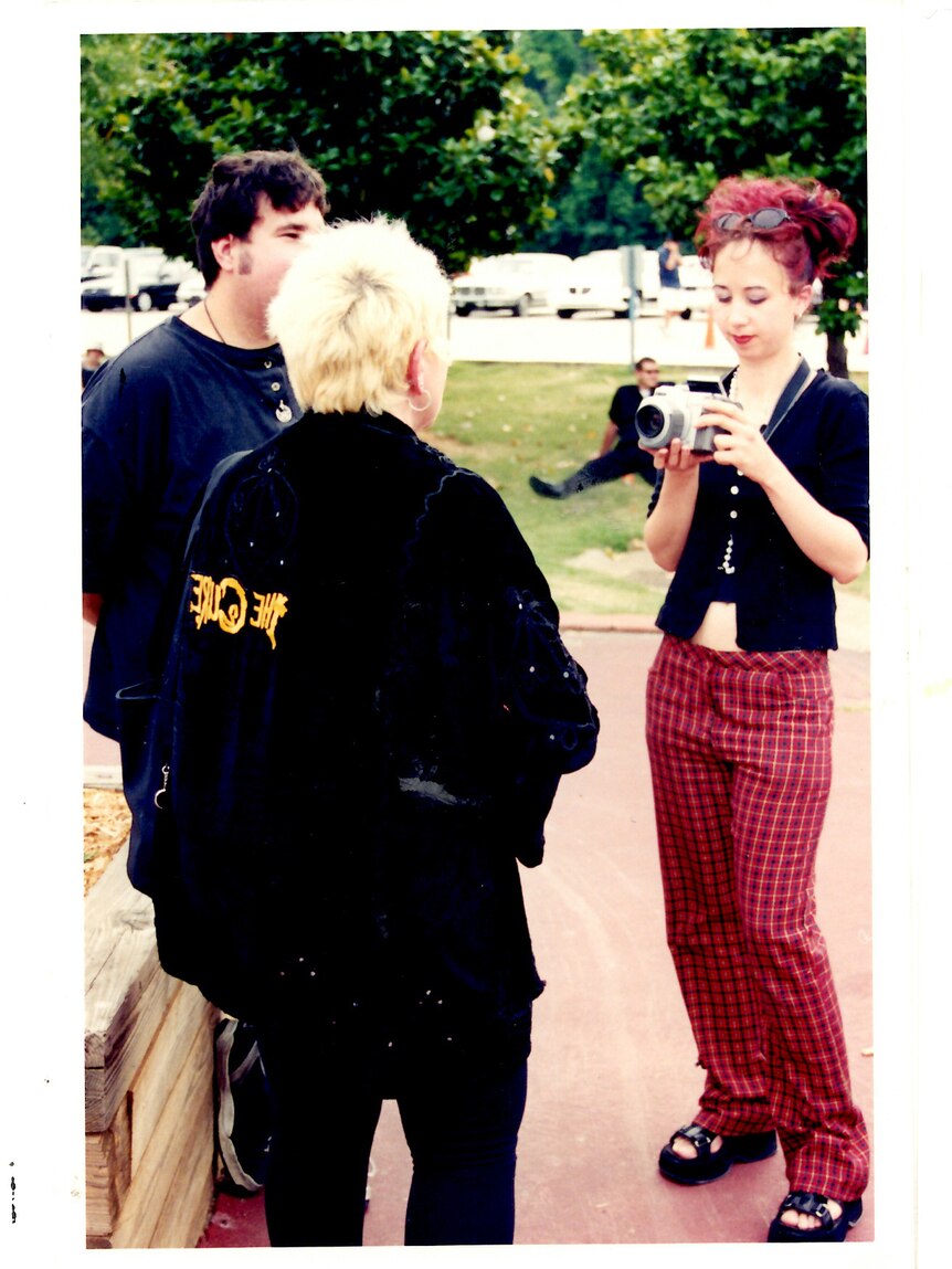 Snapshot of a woman wearing red pants and a black top filming other people 