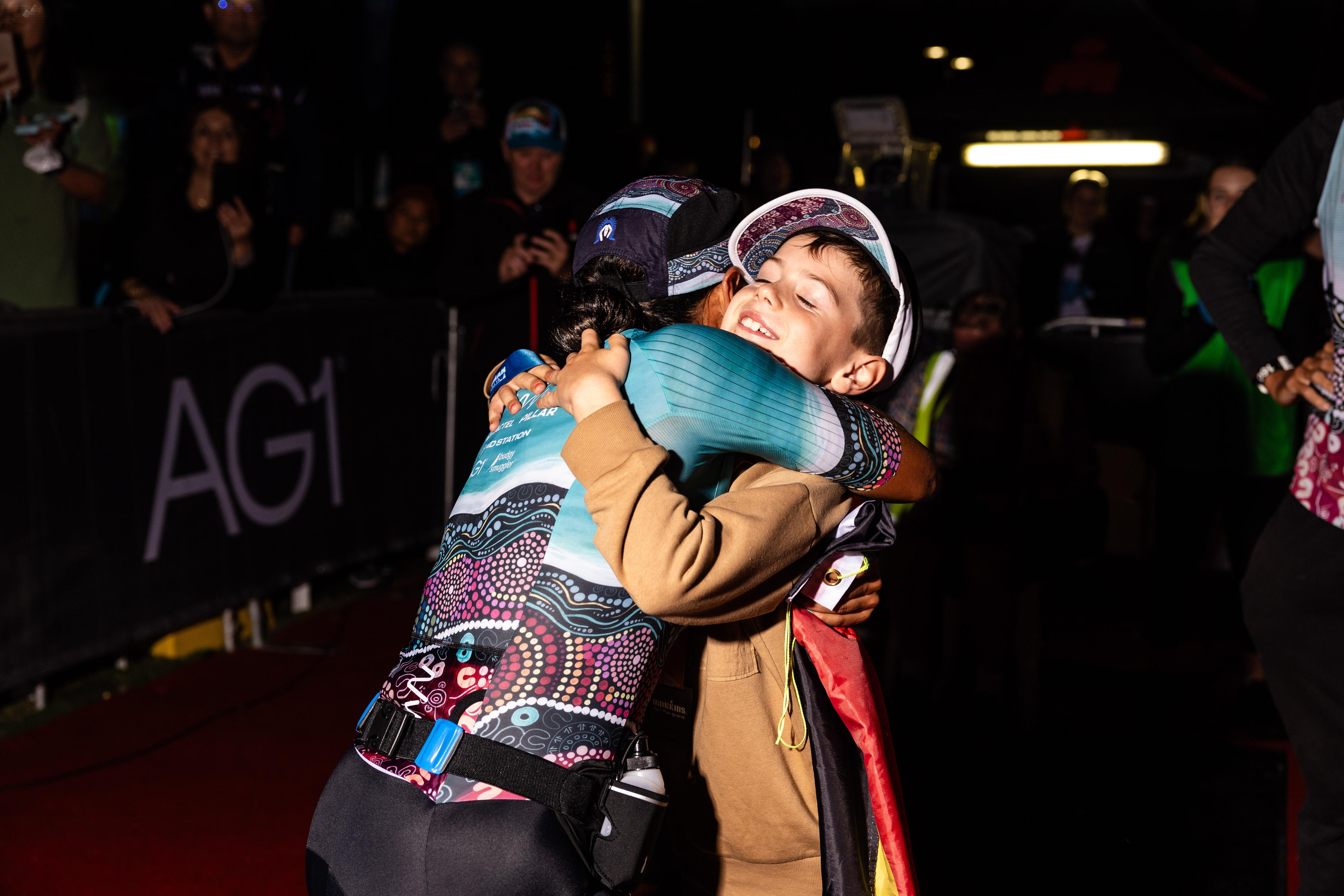 Indigenous female athlete hugs a young boy at the finish line of a triathlon race.
