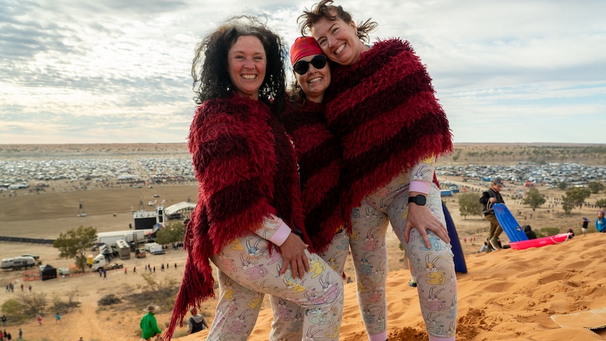 Three women in identical red and black ponchos stand on the top of the Big Red sand dune, overlooking the festival's campground