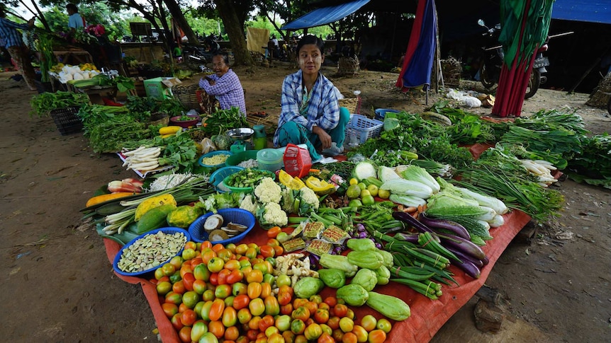 A man sits behind a table where he is selling fruits and vegatbles within myanmar's central market.