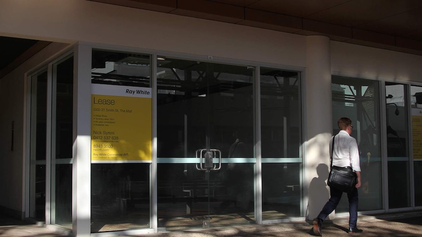 A photo of a vacant shopfront in Darwin's CBD as a man in businesswear walks past.