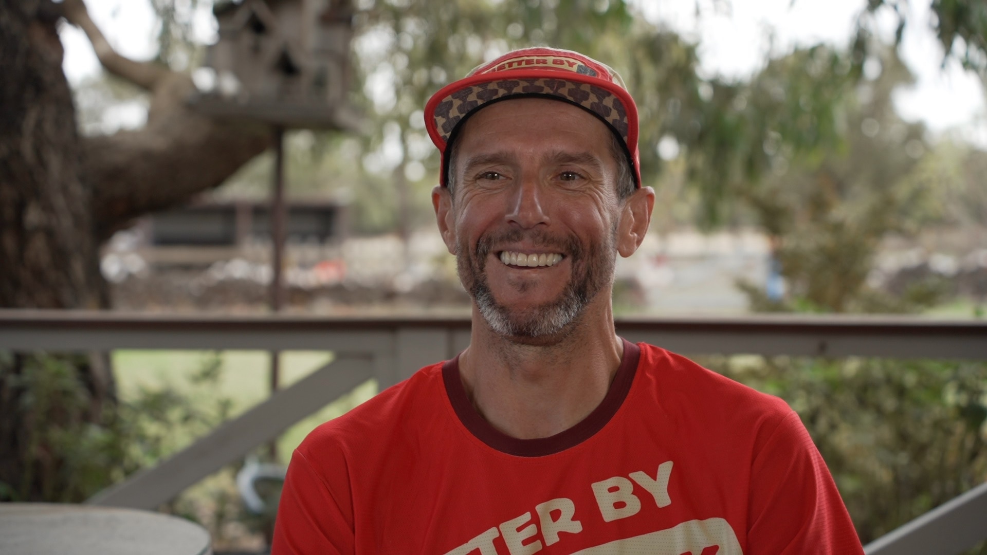 Tim Kacprzak wears a red hat and red s-hirt. He smiles at the camera.