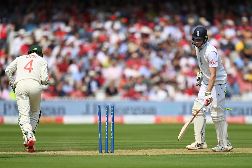 An England batsman looks down at the wicket after being stumped, as the wicketkeeper jogs away in celebration.