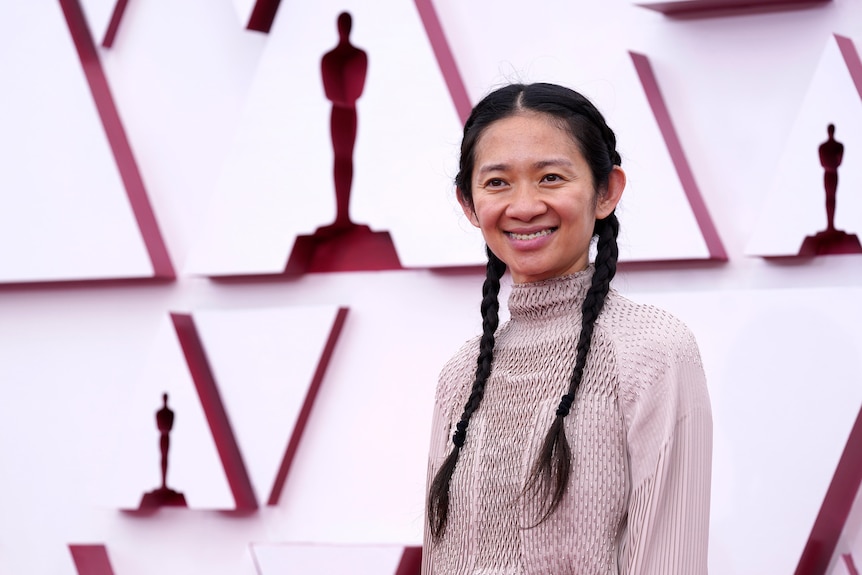 A woman smiles while posing for photos on the Oscars red carpet.