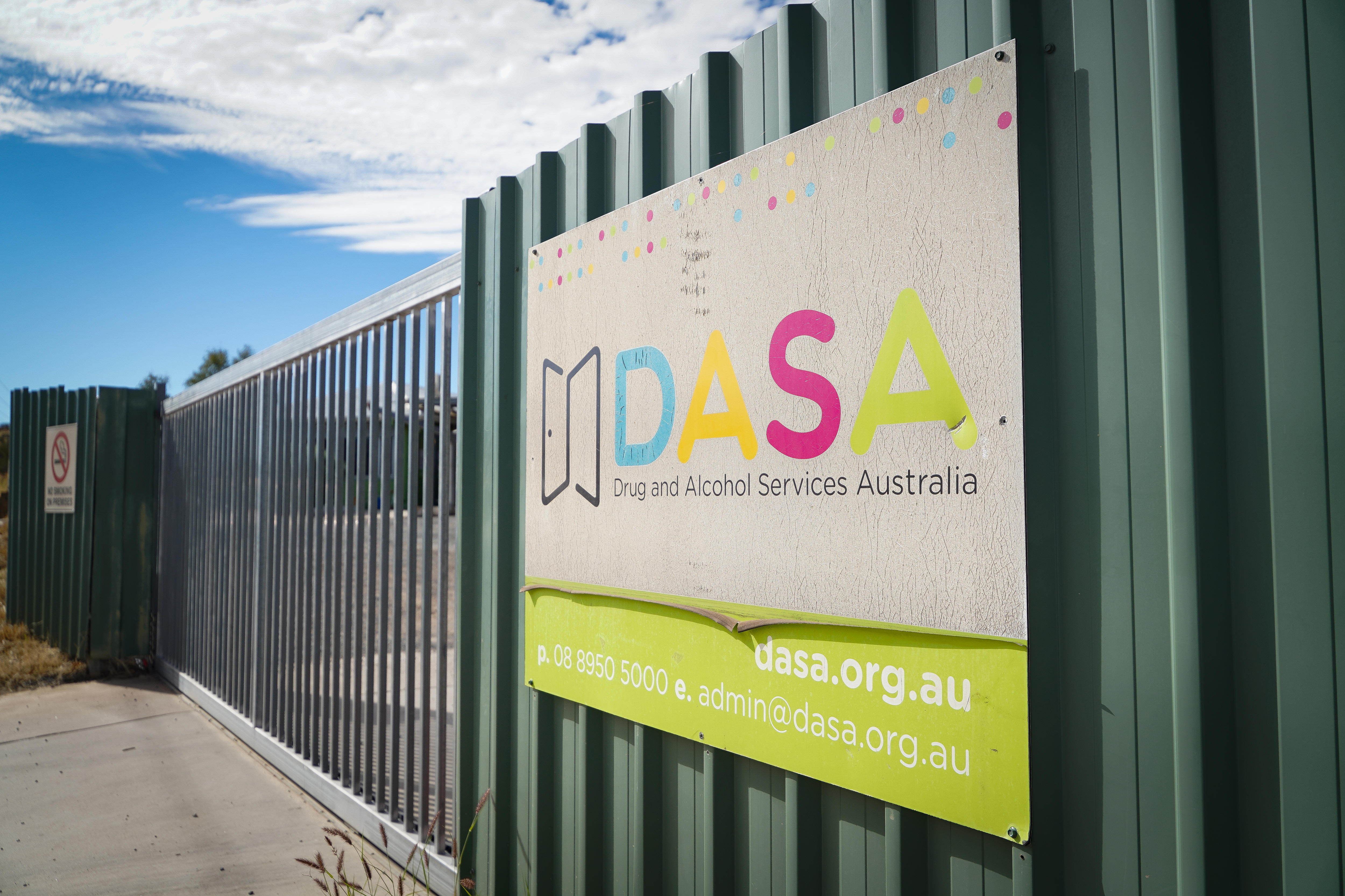 A close up of a DASA sign attached to a green fence, with a gate in the fence further back.