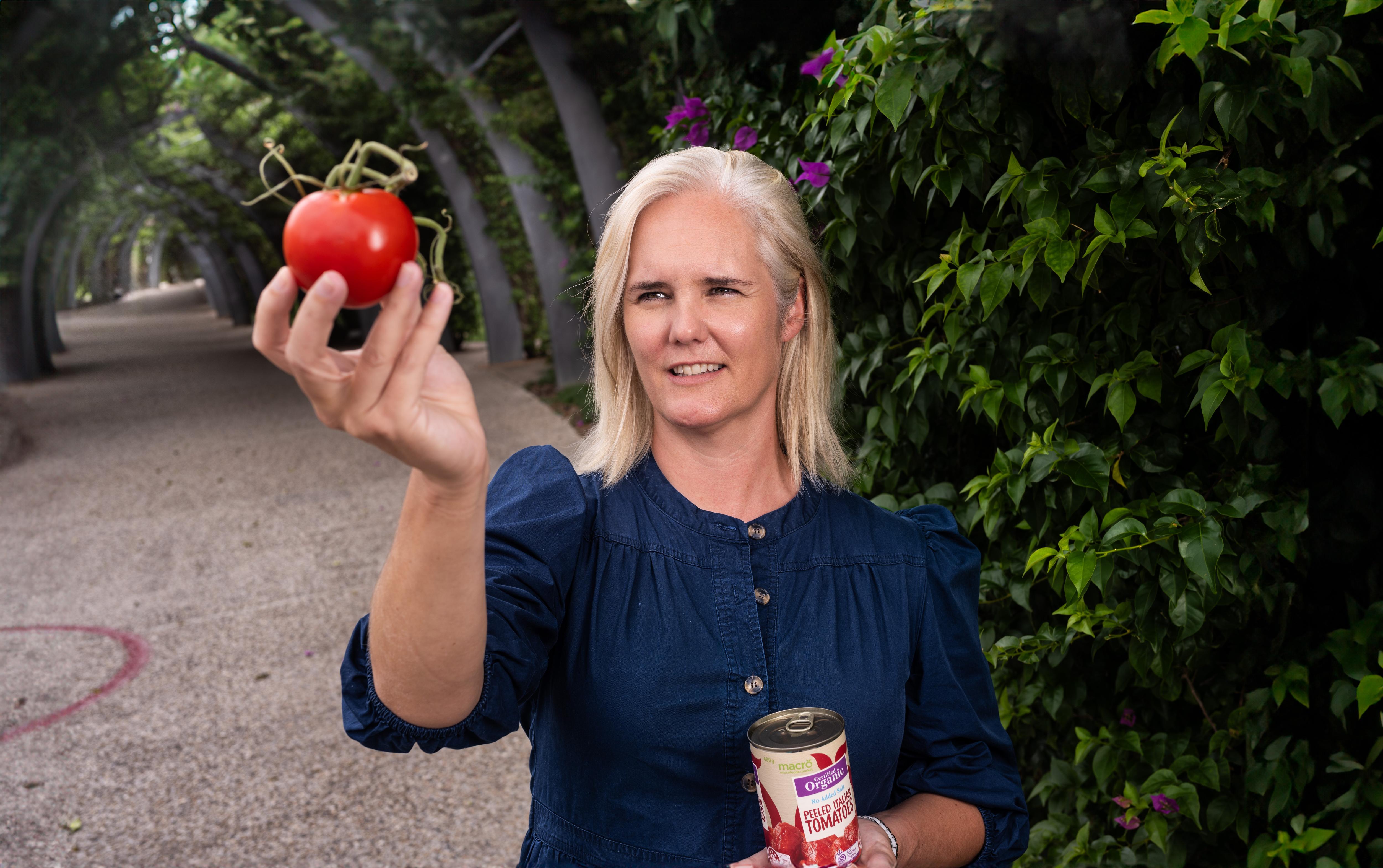 A woman inspects a tomato with a can of tomatoes in her other hand