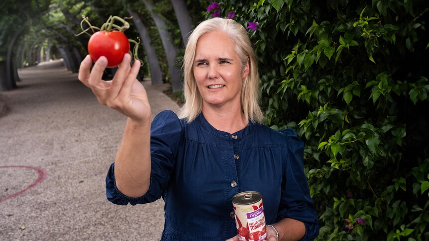 A woman inspects a tomato with a can of tomatoes in her other hand