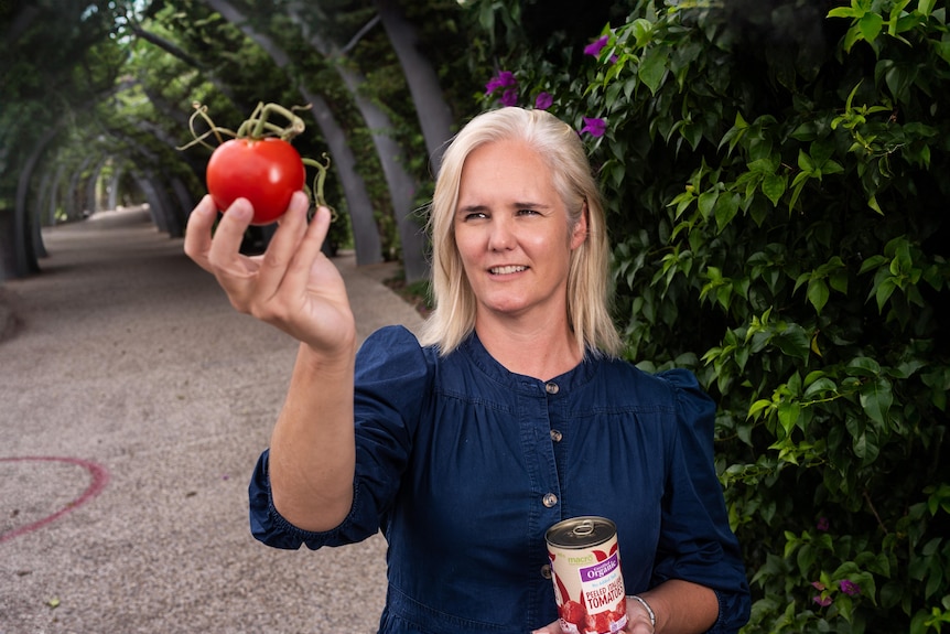 A woman inspects a tomato with a can of tomatoes in her other hand