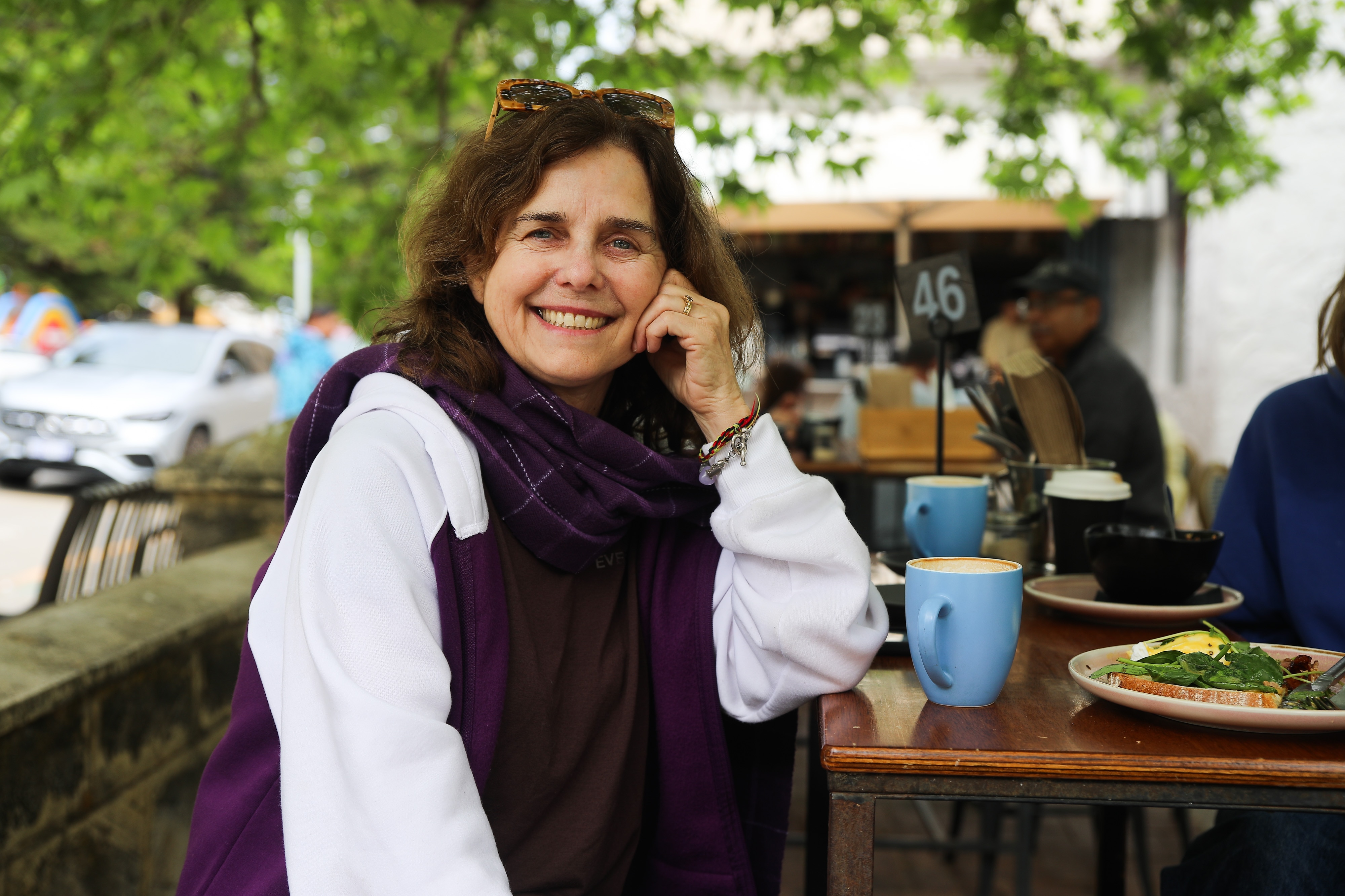 A woman leaning to a table smiles. 