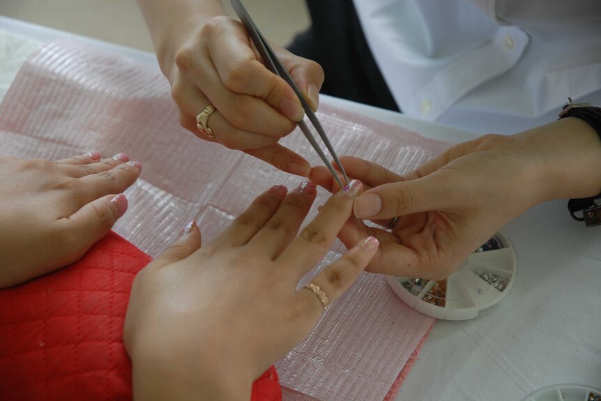 A woman has diamantes applied to her pink glittered nails