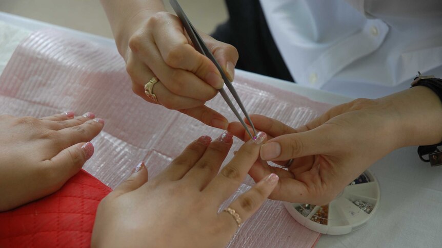 A woman has diamantes applied to her pink glittered nails