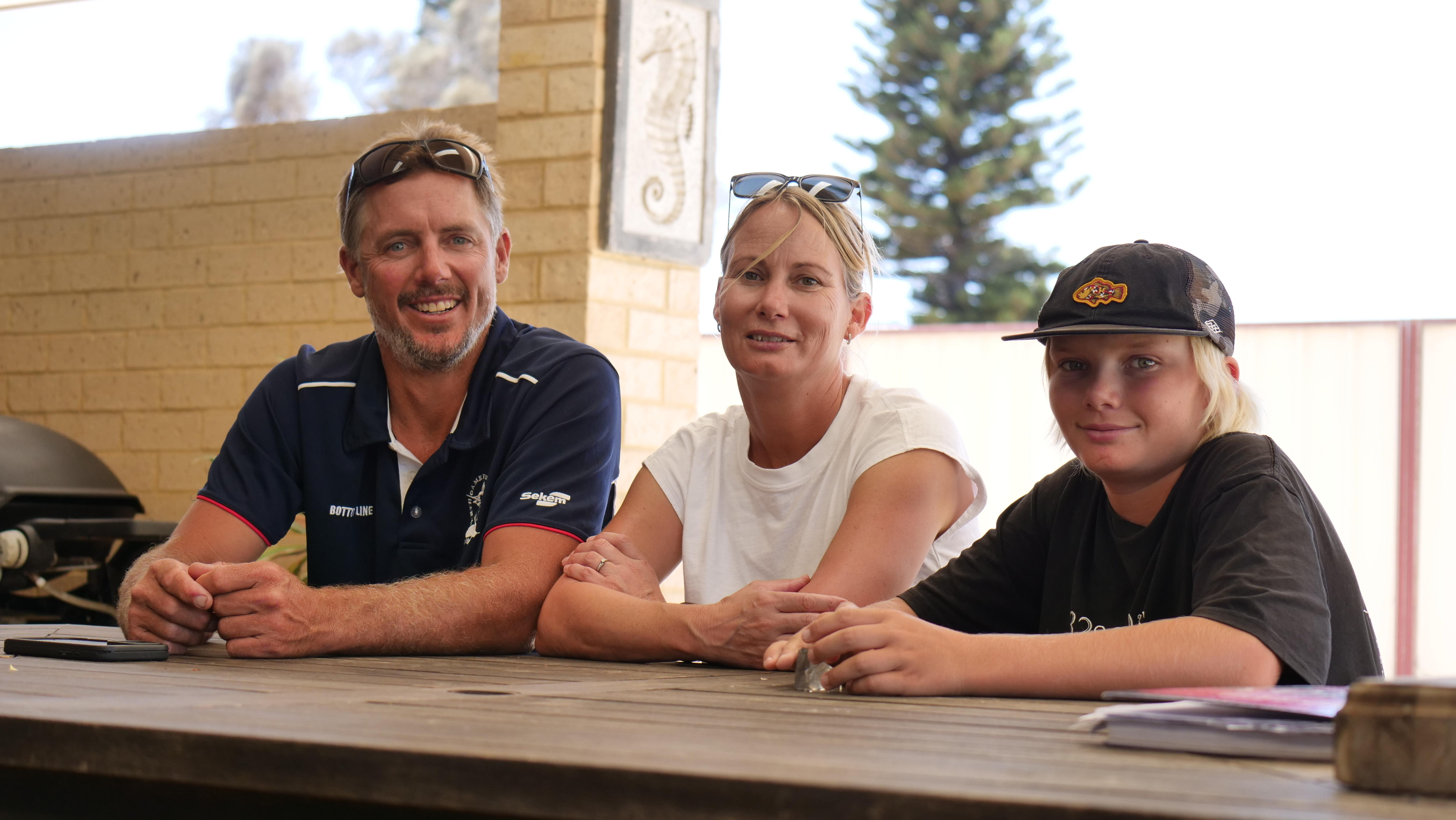 Un hombre, una mujer y un niño se sientan en una mesa y sonríen a la cámara.