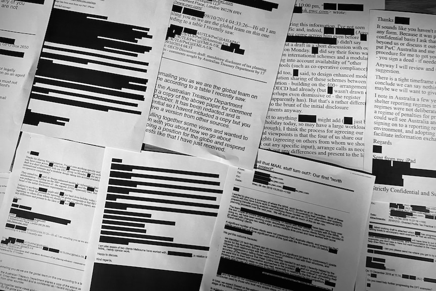 Printed black and white copies of emails laid out on a table with chunks of text redacted in black.